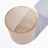 This image shows a cylindrical translucent glass candle vessel in a warm cream color. 