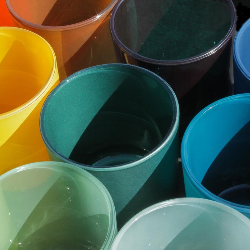 This image shows a group of empty colorful glass candle containers in the sun.