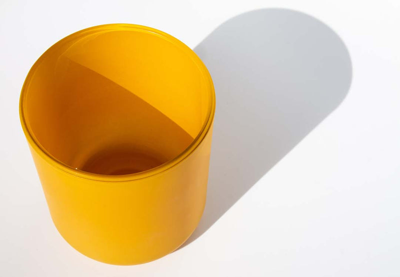 This image shows a cylindrical opaque  glass candle container in a golden yellow color.