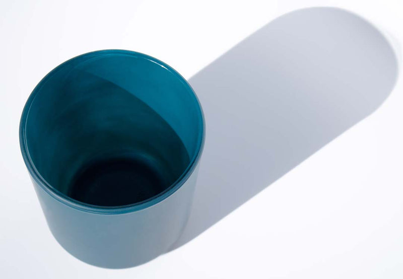 This image shows a cylindrical opaque  glass candle container in a peacock blue color.