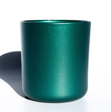 This image shows a cylindrical opaque  glass candle vessel in a metallic dark green color.